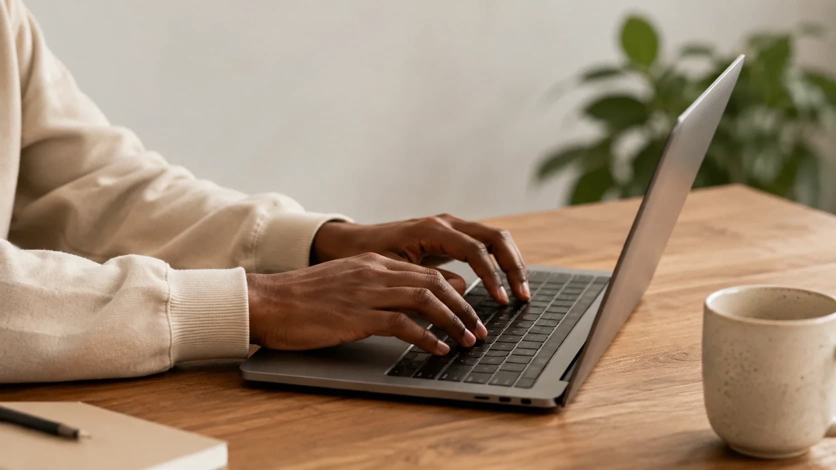 Hands using a laptop keyboard against a soft, plain background.