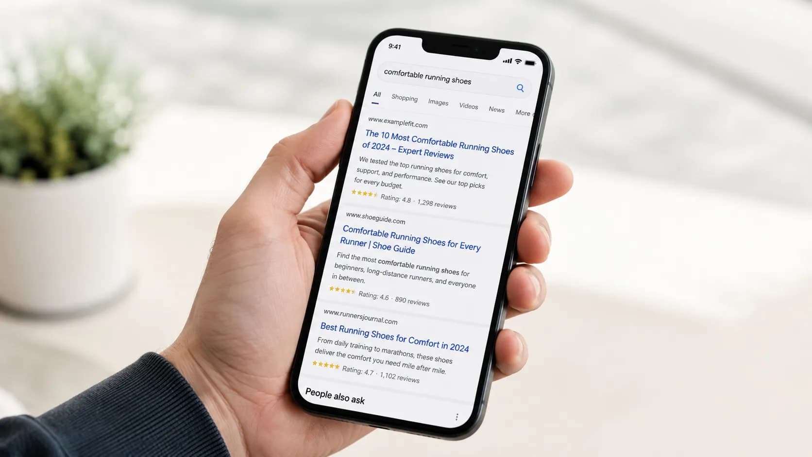 A hand holding a phone showing a page of search results.